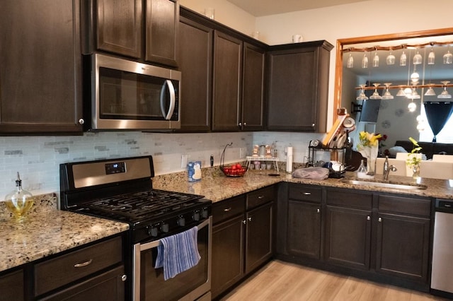 kitchen with dark brown cabinets, sink, light hardwood / wood-style flooring, stainless steel appliances, and light stone countertops