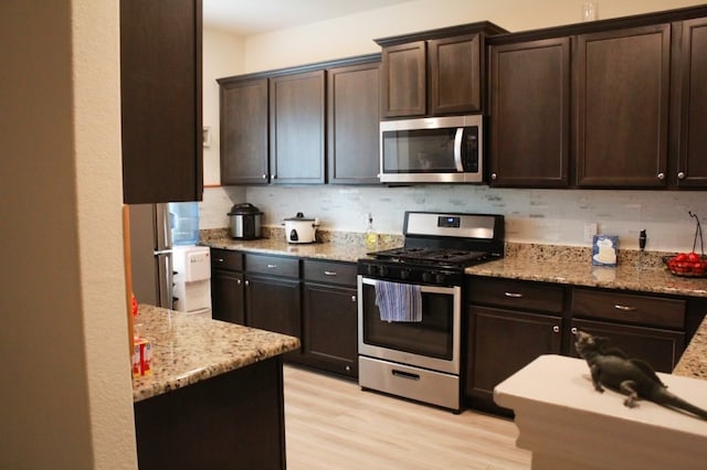 kitchen featuring dark brown cabinets, light hardwood / wood-style flooring, decorative backsplash, appliances with stainless steel finishes, and light stone countertops