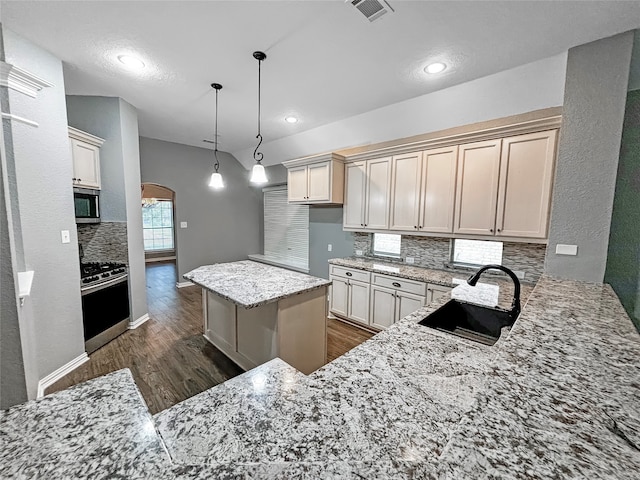 kitchen with appliances with stainless steel finishes, dark wood-type flooring, light stone countertops, pendant lighting, and a center island