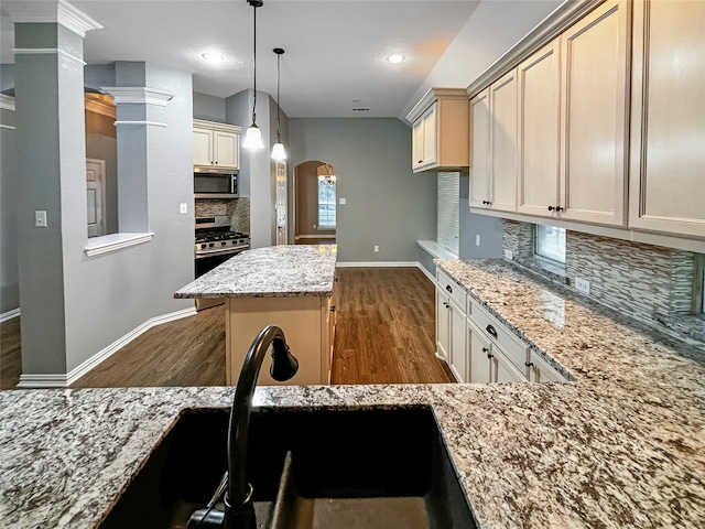 kitchen with tasteful backsplash, hanging light fixtures, cream cabinetry, stainless steel appliances, and dark hardwood / wood-style flooring