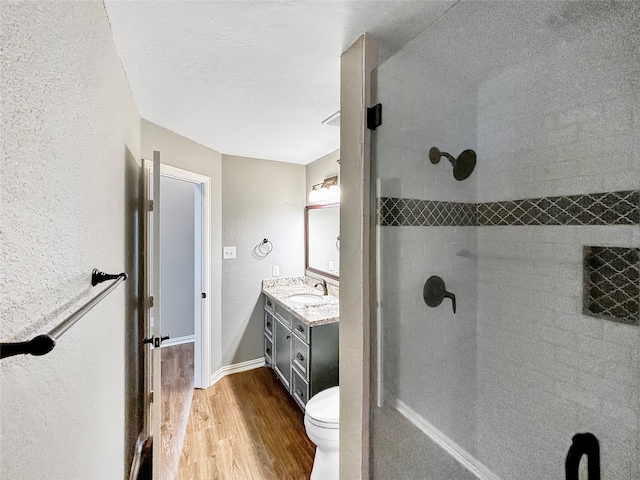 bathroom with a tile shower, wood-type flooring, a textured ceiling, vanity, and toilet