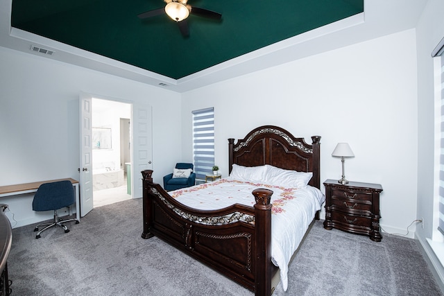 carpeted bedroom featuring a tray ceiling, ceiling fan, and ensuite bathroom