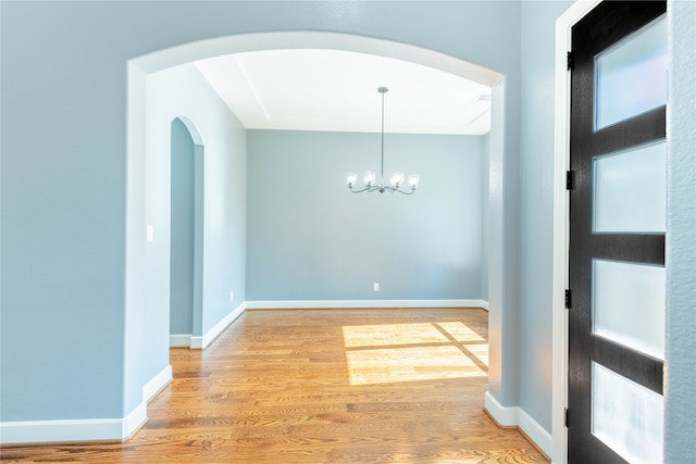 unfurnished room with an inviting chandelier and light wood-type flooring