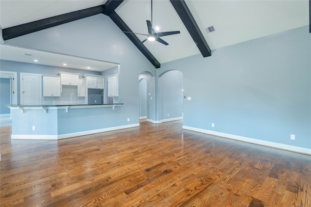 unfurnished living room featuring hardwood / wood-style flooring, beam ceiling, ceiling fan, and high vaulted ceiling