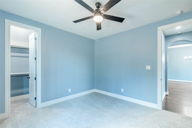 unfurnished bedroom with a spacious closet, a closet, ceiling fan, and light carpet