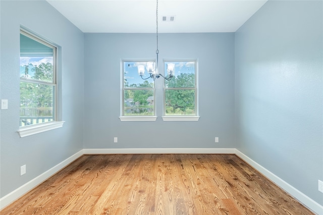 spare room with an inviting chandelier, a wealth of natural light, and light hardwood / wood-style floors