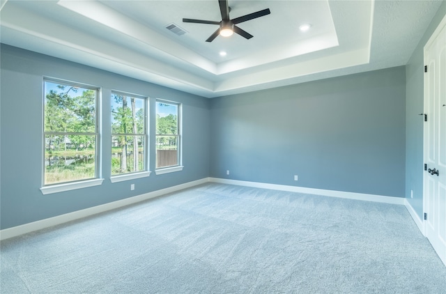 carpeted empty room with ceiling fan and a raised ceiling