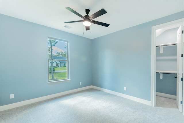 unfurnished bedroom with a closet, light colored carpet, ceiling fan, and a walk in closet