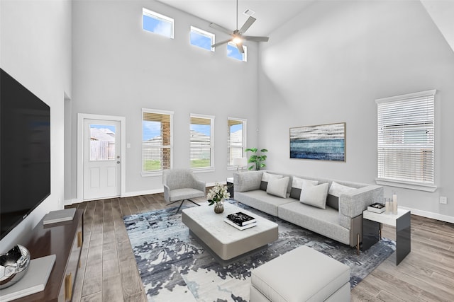 living room with a towering ceiling, hardwood / wood-style flooring, and ceiling fan