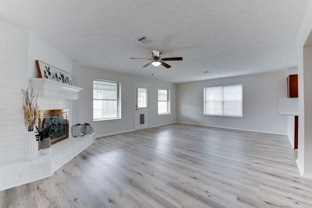 unfurnished living room with a textured ceiling, light hardwood / wood-style floors, and a brick fireplace