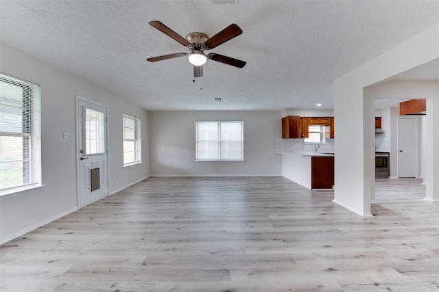 unfurnished living room featuring light hardwood / wood-style floors, ceiling fan, and a textured ceiling