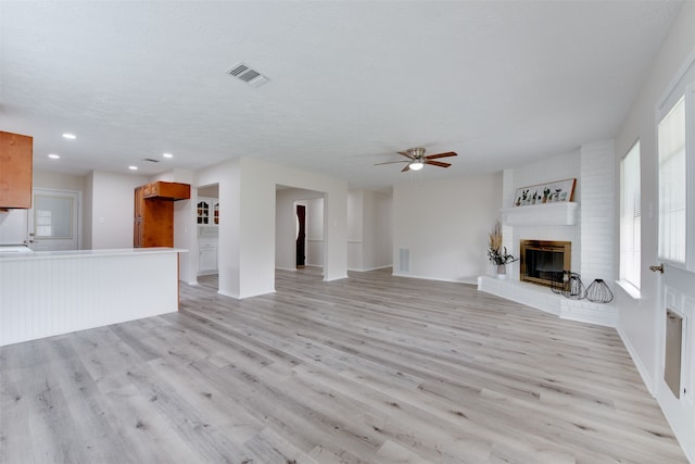 unfurnished living room featuring a brick fireplace, light wood-type flooring, a textured ceiling, and ceiling fan