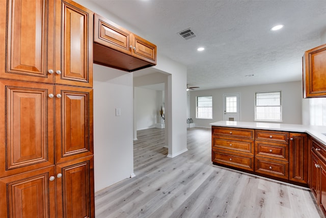 kitchen with kitchen peninsula, light hardwood / wood-style floors, a textured ceiling, and ceiling fan