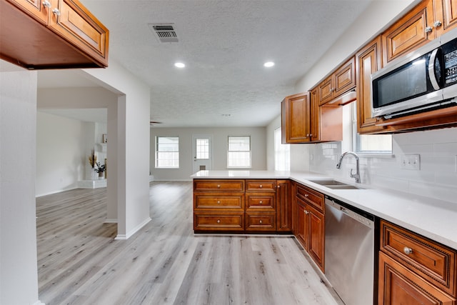 kitchen featuring light wood-type flooring, appliances with stainless steel finishes, a textured ceiling, sink, and kitchen peninsula