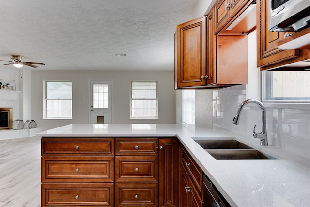 kitchen featuring sink, light stone counters, tasteful backsplash, a brick fireplace, and light wood-type flooring