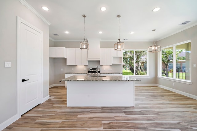 kitchen with dark stone counters, light hardwood / wood-style floors, a kitchen island with sink, sink, and white cabinets