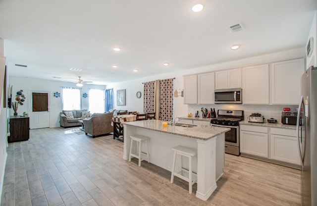 kitchen with white cabinets, a center island with sink, stainless steel appliances, and light hardwood / wood-style flooring