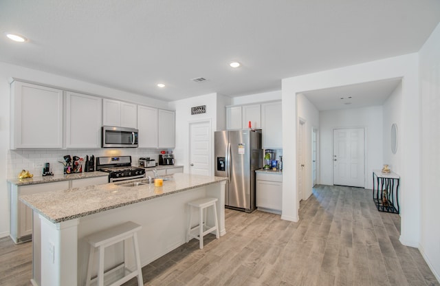 kitchen with light wood-type flooring, a kitchen island with sink, a breakfast bar area, white cabinets, and appliances with stainless steel finishes