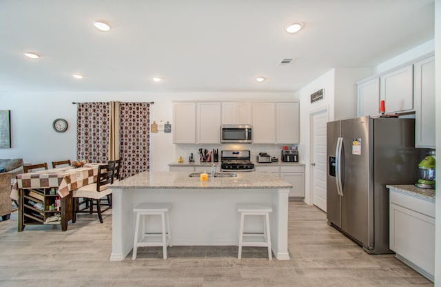 kitchen featuring a center island with sink, stainless steel appliances, light hardwood / wood-style floors, and white cabinetry