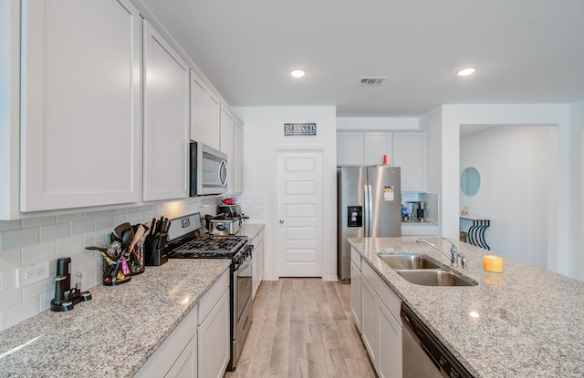 kitchen with light hardwood / wood-style floors, sink, white cabinetry, stainless steel appliances, and light stone countertops