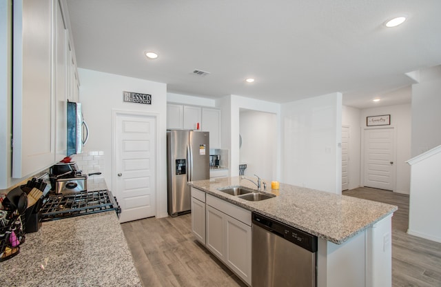 kitchen featuring an island with sink, white cabinets, stainless steel appliances, light wood-type flooring, and sink