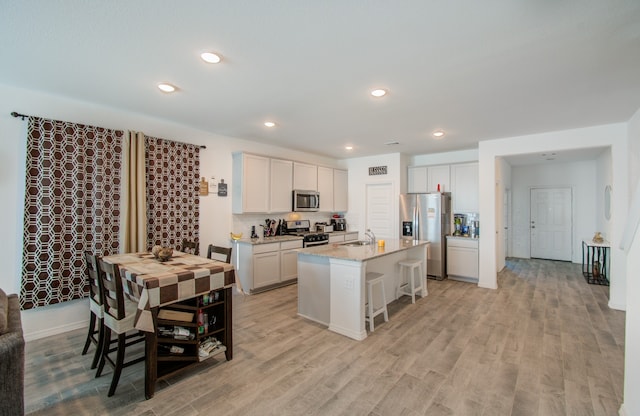 kitchen featuring an island with sink, sink, light hardwood / wood-style flooring, appliances with stainless steel finishes, and a breakfast bar