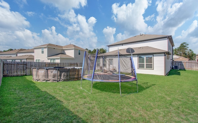 rear view of property with cooling unit, a trampoline, a yard, and a fenced in pool