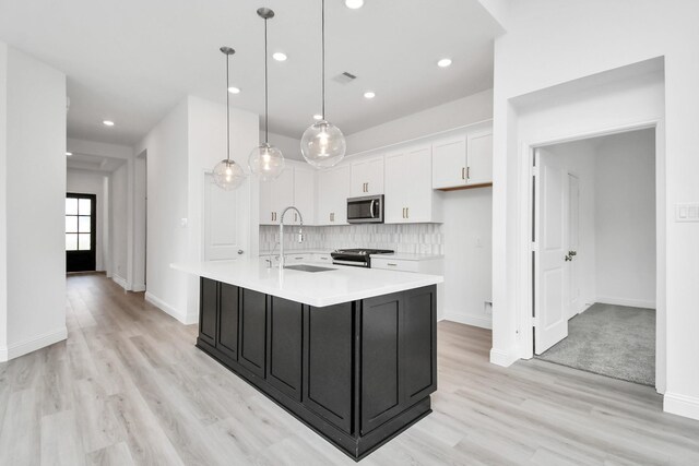 kitchen featuring white cabinets, an island with sink, hanging light fixtures, sink, and gas range oven