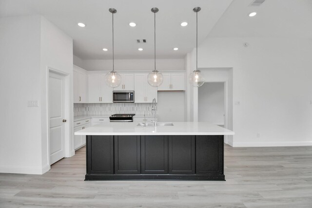 kitchen with light hardwood / wood-style floors, white cabinetry, stainless steel appliances, a center island with sink, and sink