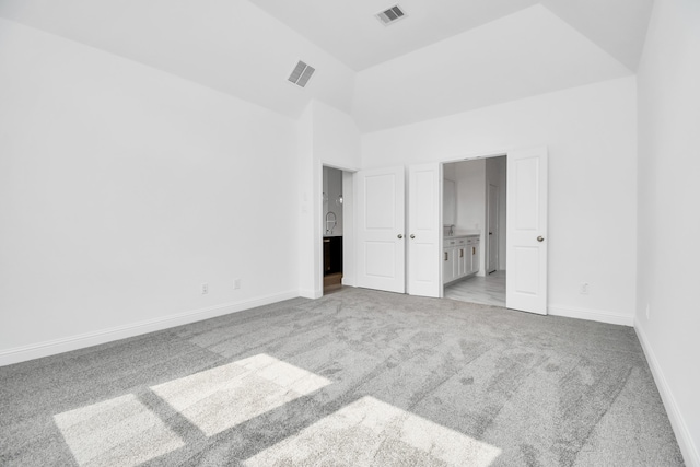 unfurnished bedroom with high vaulted ceiling, connected bathroom, and light colored carpet