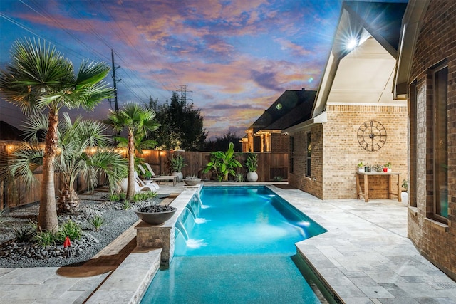 pool at dusk featuring pool water feature and a patio area