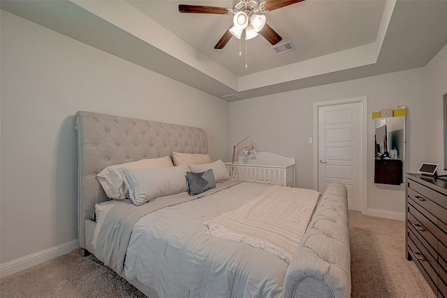 bedroom with ceiling fan, light colored carpet, and a tray ceiling