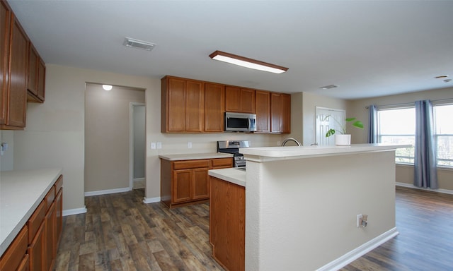 kitchen with appliances with stainless steel finishes, a center island with sink, and dark hardwood / wood-style flooring