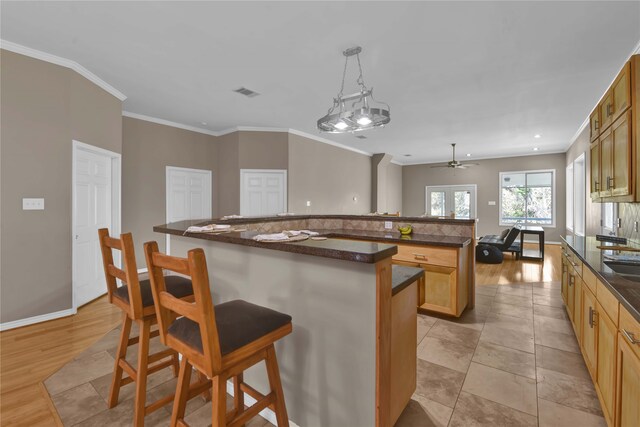 kitchen featuring a kitchen bar, a center island, light hardwood / wood-style floors, decorative light fixtures, and ornamental molding