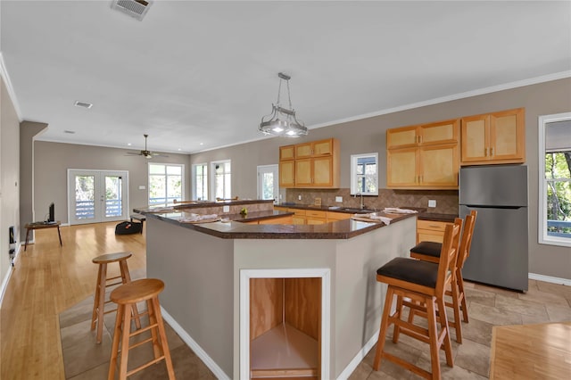 kitchen featuring a breakfast bar area, ornamental molding, sink, decorative light fixtures, and stainless steel refrigerator