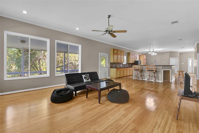 living room featuring ornamental molding, ceiling fan with notable chandelier, and light wood-type flooring