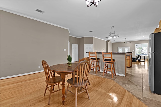 dining room with light hardwood / wood-style floors, ornamental molding, and ceiling fan with notable chandelier