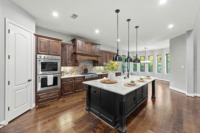 kitchen with dark brown cabinets, an island with sink, stainless steel appliances, and dark hardwood / wood-style floors