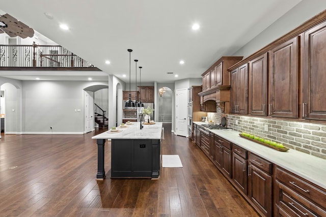 kitchen featuring tasteful backsplash, decorative light fixtures, a center island with sink, dark wood-type flooring, and a kitchen bar