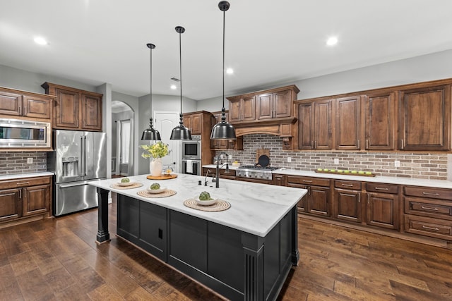 kitchen featuring a center island with sink, stainless steel appliances, dark hardwood / wood-style flooring, and decorative backsplash