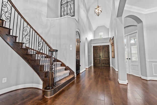 foyer entrance with a notable chandelier, ornamental molding, a high ceiling, and dark wood-type flooring