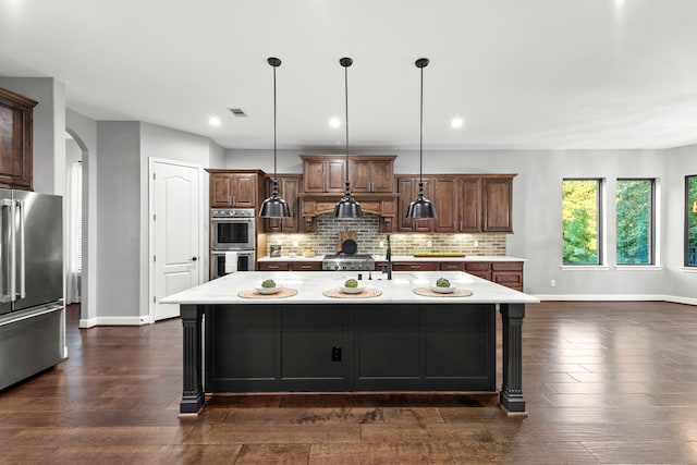 kitchen featuring decorative light fixtures, a kitchen island with sink, dark hardwood / wood-style floors, and stainless steel appliances