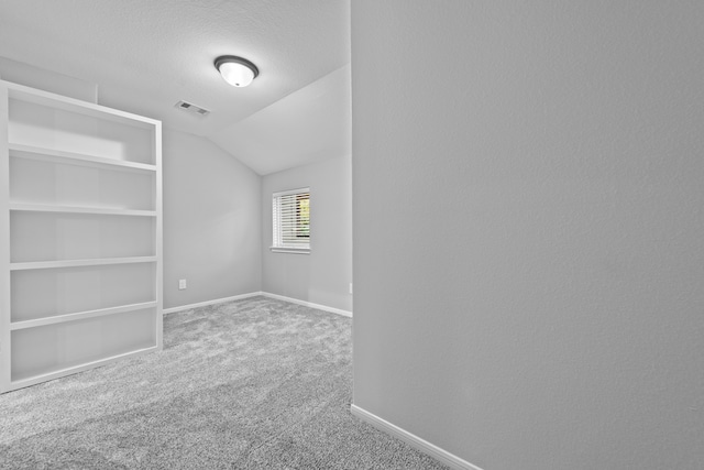 empty room with a textured ceiling, vaulted ceiling, and carpet