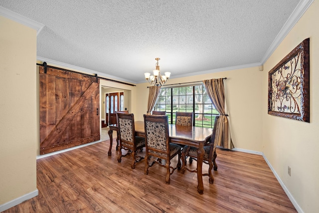 dining area with hardwood / wood-style floors, a notable chandelier, a barn door, and crown molding