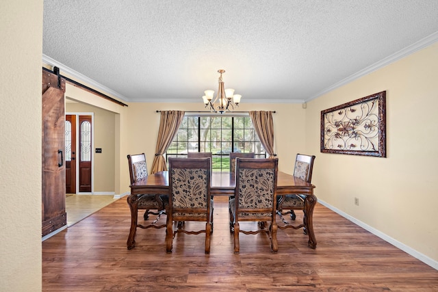 dining room featuring hardwood / wood-style flooring, a barn door, ornamental molding, and a chandelier