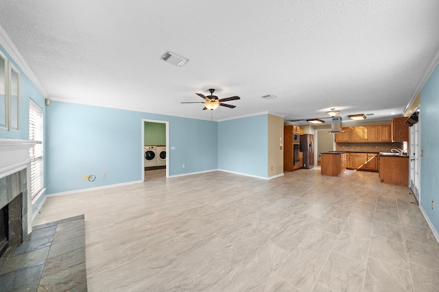 unfurnished living room featuring ceiling fan, sink, washing machine and dryer, crown molding, and a textured ceiling