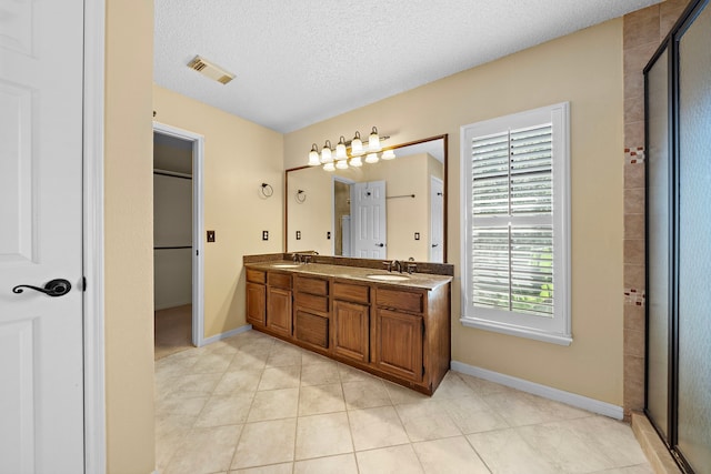 bathroom with tile patterned flooring, vanity, an enclosed shower, and a textured ceiling