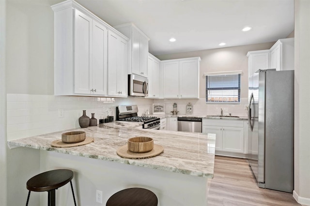 kitchen with appliances with stainless steel finishes, kitchen peninsula, a kitchen bar, and white cabinets