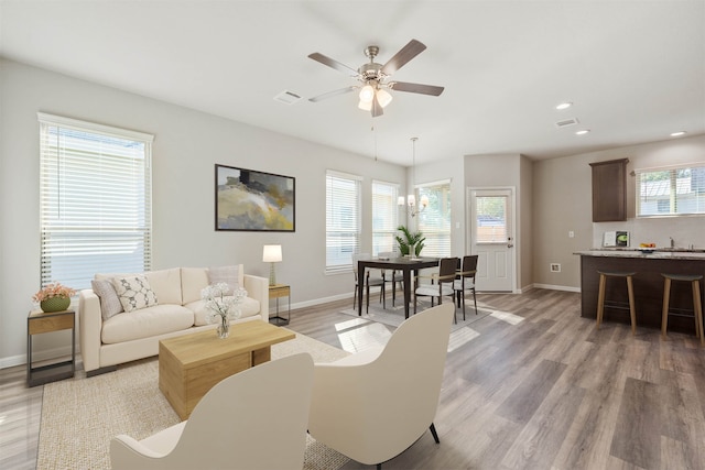 living room featuring ceiling fan with notable chandelier, light wood-type flooring, and a healthy amount of sunlight