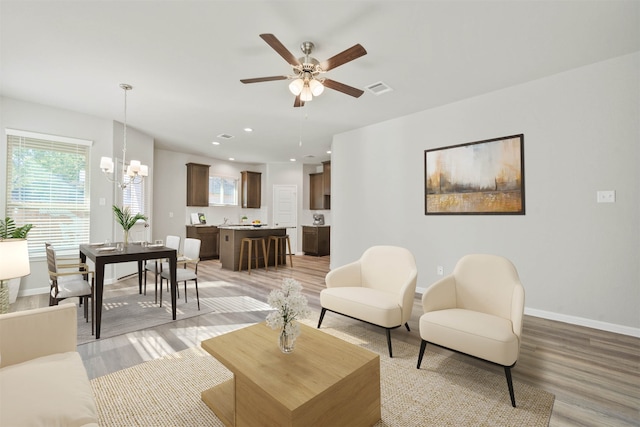 living room featuring ceiling fan with notable chandelier and light wood-type flooring